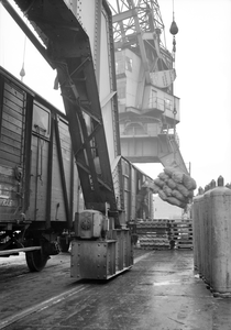 849769 Afbeelding van de overslag van goederen van trein naar schip in de haven te Rotterdam, met behulp van een havenkraan.